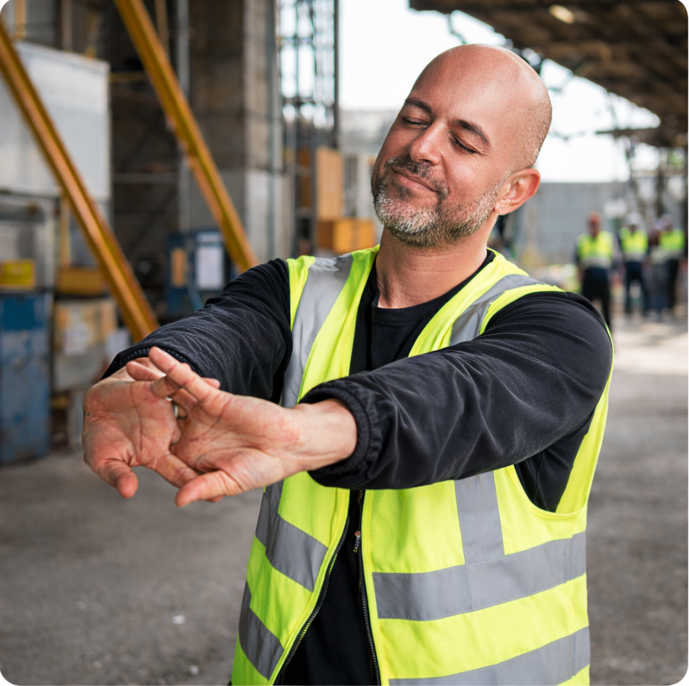 Trabalhador de colete refletivo alongando os braços no ambiente de trabalho